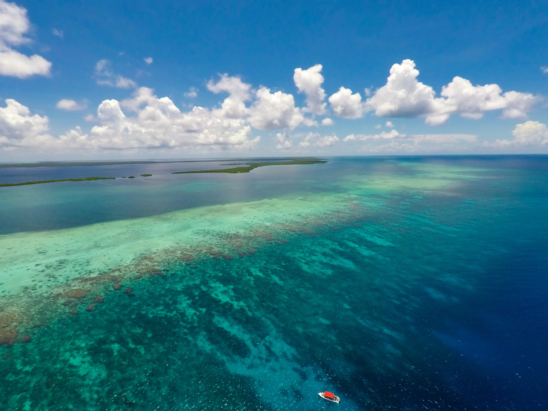 An aerial view of turquoise reef water and the coastline beneath scattered clouds